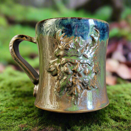 Ceramic mug with green man figure and gold handle on a gray background