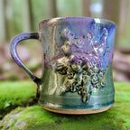 Ceramic mug with green man figure and metallic handle on a neutral background