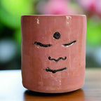 Pink ceramic mug with a face design on a plain background