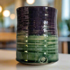 Cylindrical ceramic vase with purple and green glaze on a white background