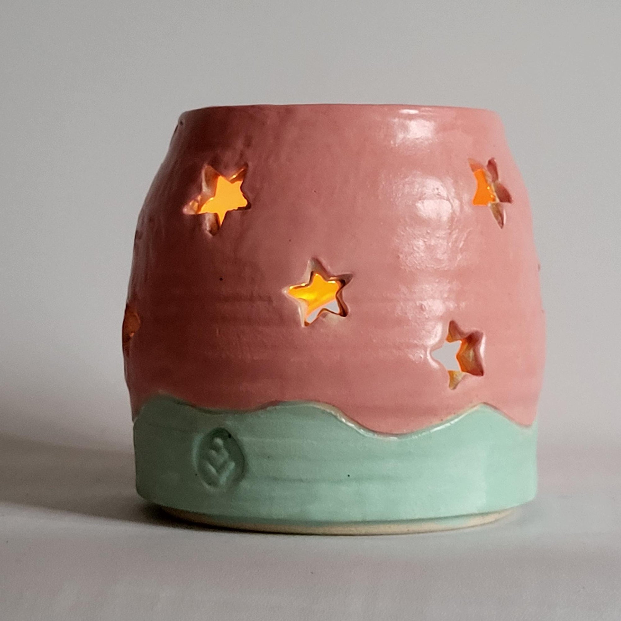 Tea light candle holder with star cutouts and pink and aqua glaze
