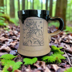 Ceramic mug with black handle and beige body featuring a printed design on a neutral background