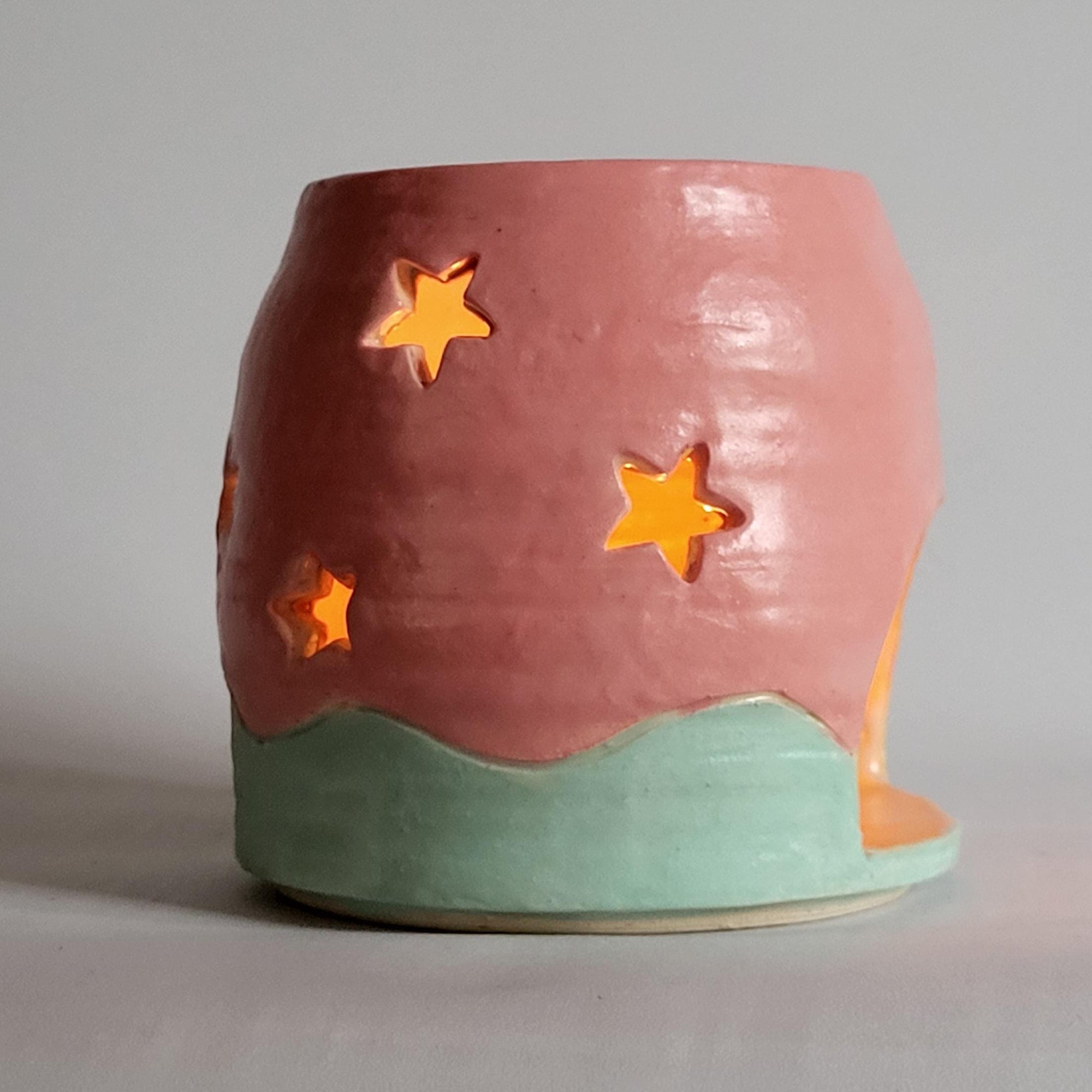 Tea light candle holder with star cutouts and pink and aqua glaze