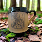 Ceramic mug with a black handle and a decorative design on a neutral background