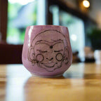 Pink ceramic cup with a face design on a gray background