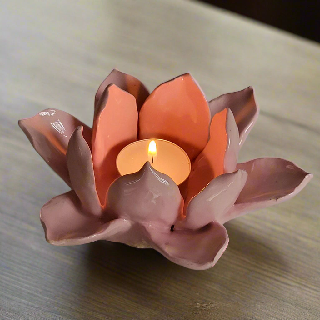 Pink ceramic lotus flower candle holder with a lit candle on a gray background